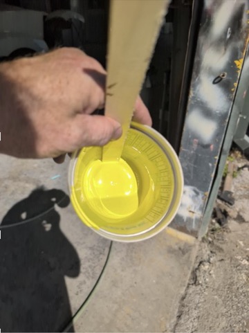 Yellow paint sample being stirred in a mixing cup